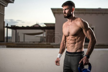 Photo for Muscular shirtless man holding kettlebell and preparing for weight training outdoors. - Royalty Free Image