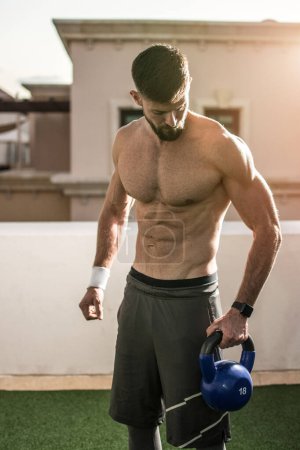 Photo for Portrait of muscular shirtless man holding kettle bell and preparing for weight training outdoors. - Royalty Free Image