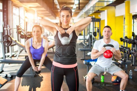 Téléchargez les photos : Groupe de trois jeunes sportifs ayant un entraînement de fitness fonctionnel avec kettlebell en salle de gym - en image libre de droit