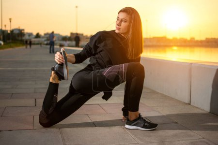 Foto de Mujer joven fitness en ropa deportiva calentándose antes de correr al aire libre durante el atardecer - Imagen libre de derechos