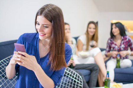 Photo for Young woman using smartphone while sitting with friends at home - Royalty Free Image
