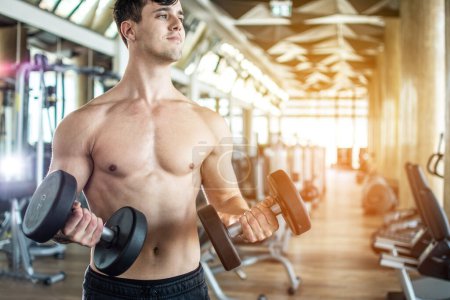 Photo for Handsome shirtless weightlifter working out with dumbbells at gym - Royalty Free Image