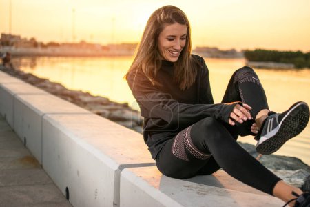 Téléchargez les photos : Joyeux jeune femme de remise en forme qui se réchauffe à l'extérieur pendant le coucher du soleil portant des vêtements de sport - en image libre de droit
