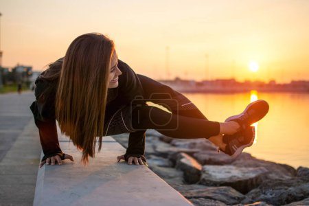 Téléchargez les photos : Ajustement jeune femme pratiquant le yoga, faisant bras stand Astavakrasana, équilibre asymétrique bras Huit Angle Pose près de la côte de la mer pendant le coucher du soleil. - en image libre de droit