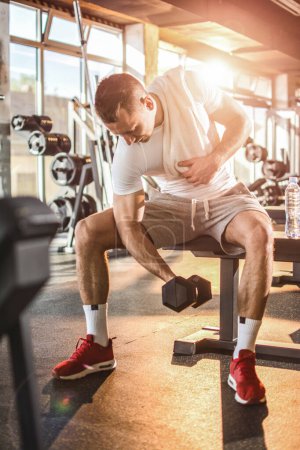 Téléchargez les photos : Jeune homme beau soulevant des poids dans la salle de gym - en image libre de droit