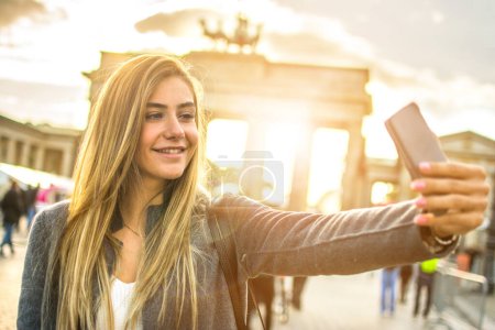 Foto de Mujer rubia bonita tomando una selfie frente a la Puerta de Brandeburgo en Berlín, Alemania. - Imagen libre de derechos