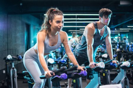 Photo for Attractive woman and handsome man doing spinning on cycling bikes. - Royalty Free Image