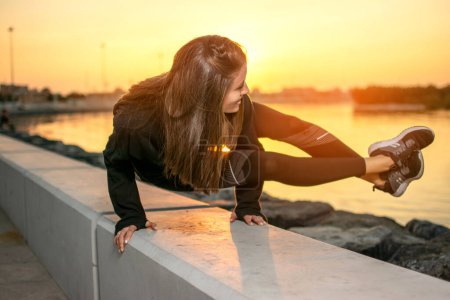 Téléchargez les photos : Fit jeune femme pratiquant le yoga, faisant bras stand Astavakrasana, équilibre asymétrique bras Huit Angle Pose près de la côte de la mer pendant le coucher du soleil. - en image libre de droit