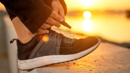 Téléchargez les photos : Gros plan de coureuses mains attachant ses chaussures avant de courir dehors devant le coucher du soleil - en image libre de droit