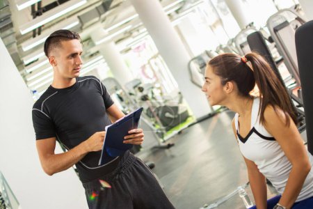 Téléchargez les photos : Entraîneur personnel expliquant les résultats de l'exercice à sa cliente dans une salle de gym. - en image libre de droit