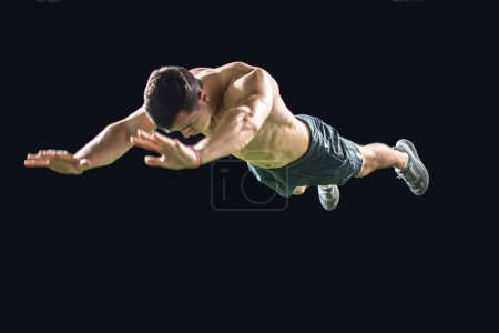 Foto de Joven musculoso haciendo flexiones con saltos aislados sobre fondo negro. - Imagen libre de derechos