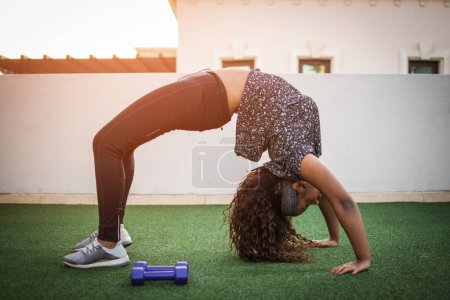 Photo for Slim attractive African-ameican young woman in sportswear exercising in Urdhva Dhanurasana pose at rooftop gym. - Royalty Free Image