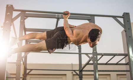 Téléchargez les photos : Homme musclé faisant des exercices sur la barre horizontale suspendue à une main. Séance d'entraînement en Calisthénique. - en image libre de droit