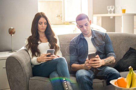 Junges Paar ruht sich auf Sofa aus und nutzt Smartphone getrennt