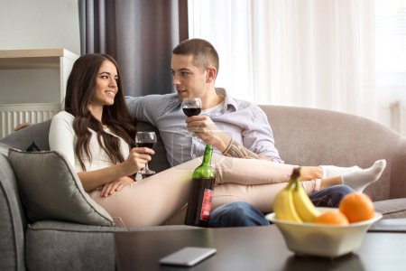 Téléchargez les photos : Jeune couple reposant sur un canapé et buvant du vin rouge - en image libre de droit