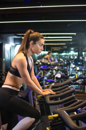 Téléchargez les photos : Une jeune sportive s'entraîne sur un vélo d'appartement dans une salle de gym. - en image libre de droit
