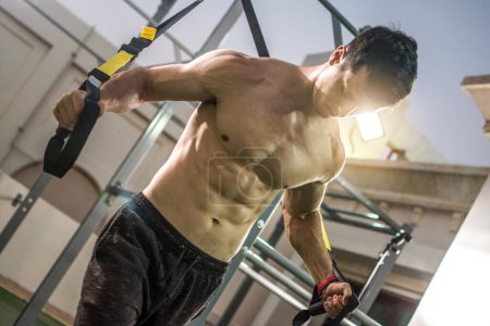 Foto de Deportista musculoso sin camisa haciendo ejercicio con correas de suspensión en el gimnasio. - Imagen libre de derechos