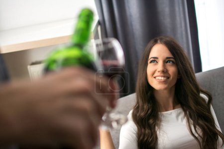 Photo for Young beautiful woman looking at her boyfriend while he is pouring wine for her - Royalty Free Image
