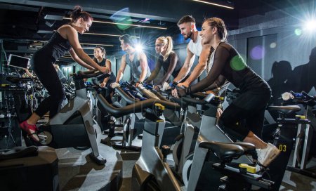 Photo for Sporty people on riding exercise bikes with assistance of their trainer during cycling class. - Royalty Free Image
