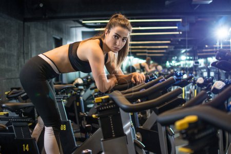Foto de Vista lateral de la joven deportista entrenando en bicicleta estática en el gimnasio. - Imagen libre de derechos