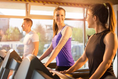 Téléchargez les photos : Amis faisant de l'exercice ensemble sur tapis roulant en salle de gym - en image libre de droit