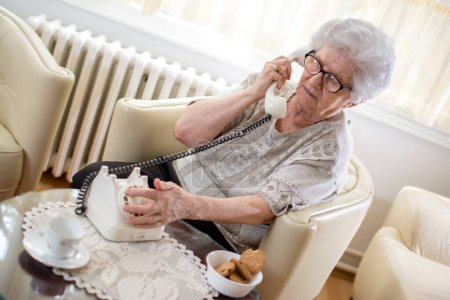 Photo for Senior woman using rotary phone at home. - Royalty Free Image
