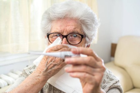 Téléchargez les photos : Femme âgée vérifiant la température corporelle avec thermomètre et nez soufflant. - en image libre de droit