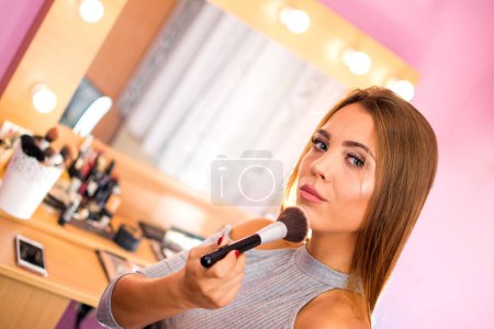 Téléchargez les photos : Jeune femme appliquant cosmétique avec une grande brosse. - en image libre de droit