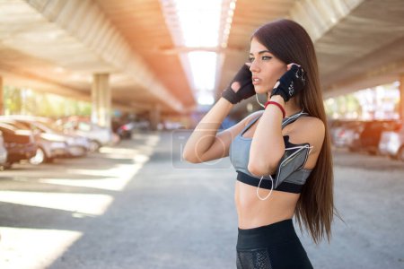 Foto de Chica deportiva en ropa deportiva escuchando música con auriculares después de entrenar al aire libre - Imagen libre de derechos