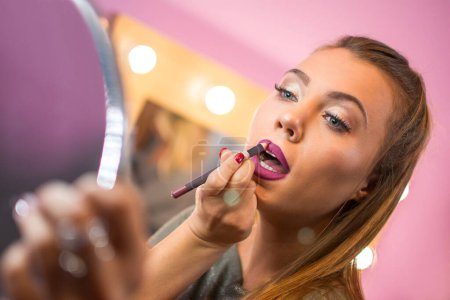 Photo for Beautiful young woman with mirror putting on lip liner. - Royalty Free Image