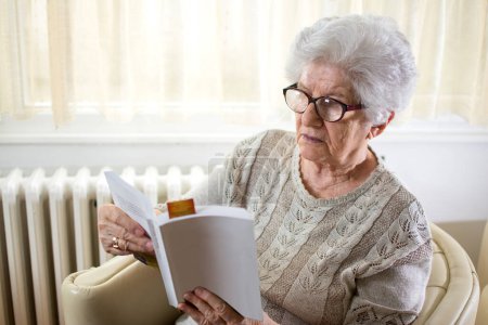 Foto de Mujer mayor leyendo libro en casa. - Imagen libre de derechos