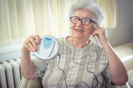 Cheerful senior woman listening to music on CD player at home.