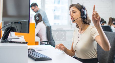 Foto de Operadora de centro de llamadas femenino joven con auriculares manos libres hablando con el cliente en la oficina. - Imagen libre de derechos