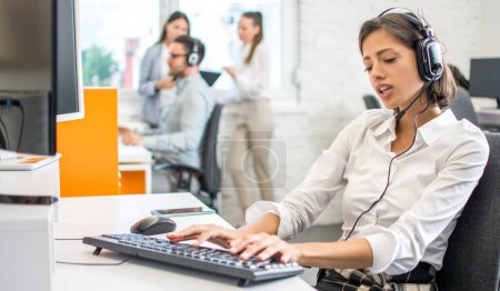 Téléchargez les photos : Belle opérateur de centre d'appels féminin travaillant sur ordinateur dans le bureau. - en image libre de droit