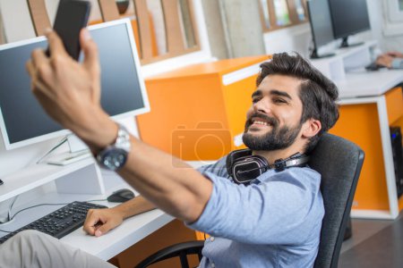 Téléchargez les photos : Beau jeune homme prenant un selfie sur le lieu de travail. - en image libre de droit