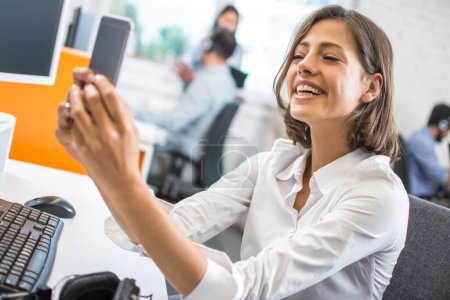 Téléchargez les photos : Gros plan portrait de jolie jeune femme d'affaires souriante prenant un selfie dans un bureau. - en image libre de droit