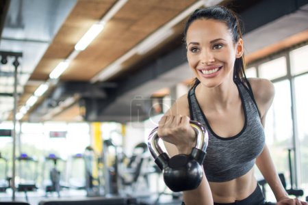 Téléchargez les photos : Souriant jeune femme travaillant avec cloche de bouilloire dans la salle de gym. - en image libre de droit