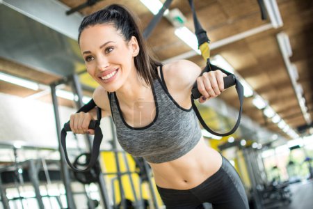 Atleta mujer haciendo flexiones con correas de fitness trx en el gimnasio.