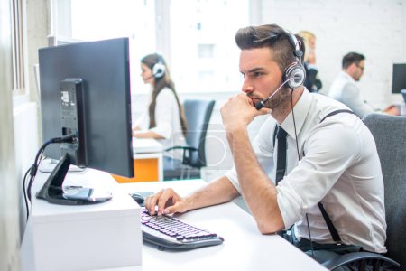 Foto de Hombre de negocios pensativo con auriculares en el lugar de trabajo en la oficina delante de la computadora - Imagen libre de derechos