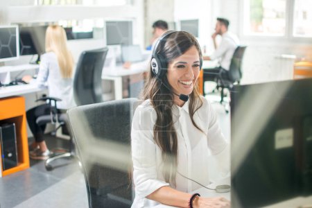 Photo for Beautiful smiling woman with headphones using computer while counseling at call center - Royalty Free Image