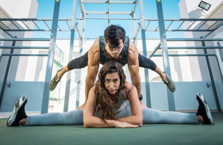 Photo for Young woman in sportswear doing the splits while man doing handstand over her thighs outdoors - Royalty Free Image