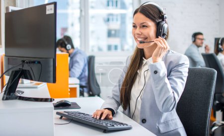 Photo for Friendly female helpline operator in call center. Young woman working in call center and holding microphone on headset with hand. - Royalty Free Image