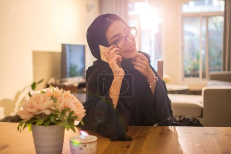 Foto de Retrato de una bonita mujer árabe de Oriente Medio hablando por teléfono móvil en casa. - Imagen libre de derechos