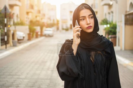Téléchargez les photos : Portrait d'une belle femme d'affaires arabe portant du hijab parlant sur un téléphone portable dans la rue de la ville. - en image libre de droit