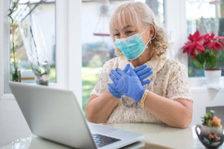 Photo for Scared mid age woman wearing protective mask and gloves reading news on laptop at home. Stay at home, pandemic concept. - Royalty Free Image
