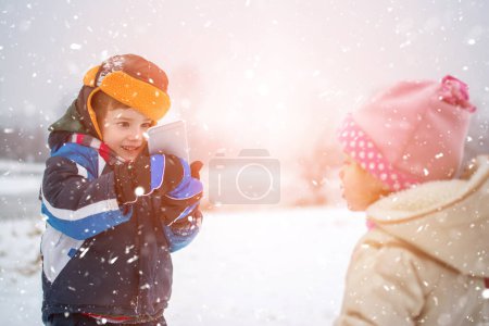 Photo for Little boy taking photo of his little sister on mobile phone during snowy winter day - Royalty Free Image