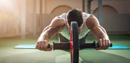 Téléchargez les photos : Vue panoramique de l'homme musclé faisant de l'exercice avec un rouleau abdominal dans la salle de gym. - en image libre de droit