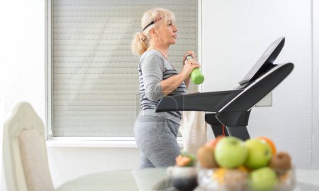 Photo for Active senior woman in sportswear walking on treadmill at home. - Royalty Free Image