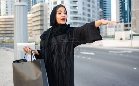 Foto de Hermosa mujer musulmana con bolsas de compras tratando de coger un taxi en la calle de la ciudad - Imagen libre de derechos