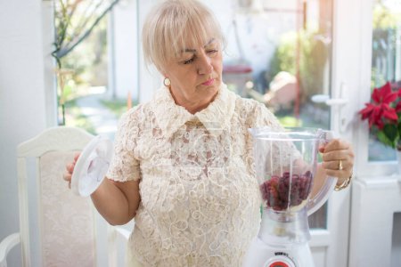 Foto de Retrato de mujer mayor preparando batido orgánico vegano, usando licuadora en la cocina. - Imagen libre de derechos